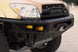 Close-up of a black off-road front bumper with integrated amber lights and a winch, mounted on a tan Toyota Tundra V8 truck.