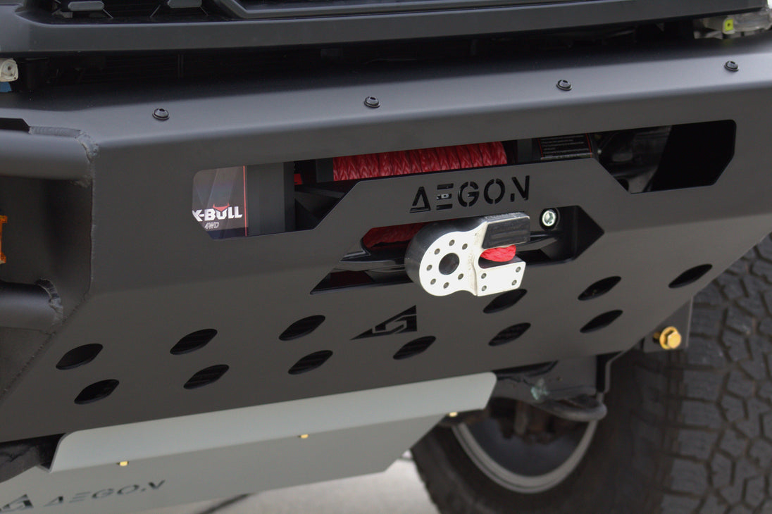 Close-up of a black metal front bumper with a winch mounted on it, featuring the AEGON brand name on the bumper and a winch housing with red and white components.