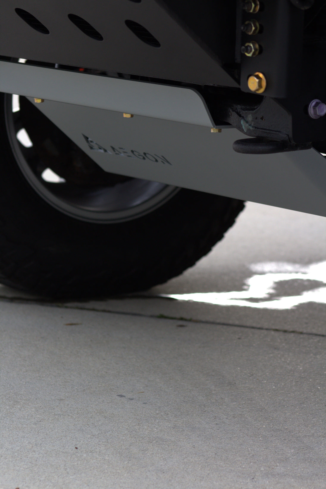 Close-up of a vehicle undercarriage showing a black tire, a dark metal frame, and a gray metal skid plate with the brand name 'Kubota' embossed on it, set on a concrete surface.