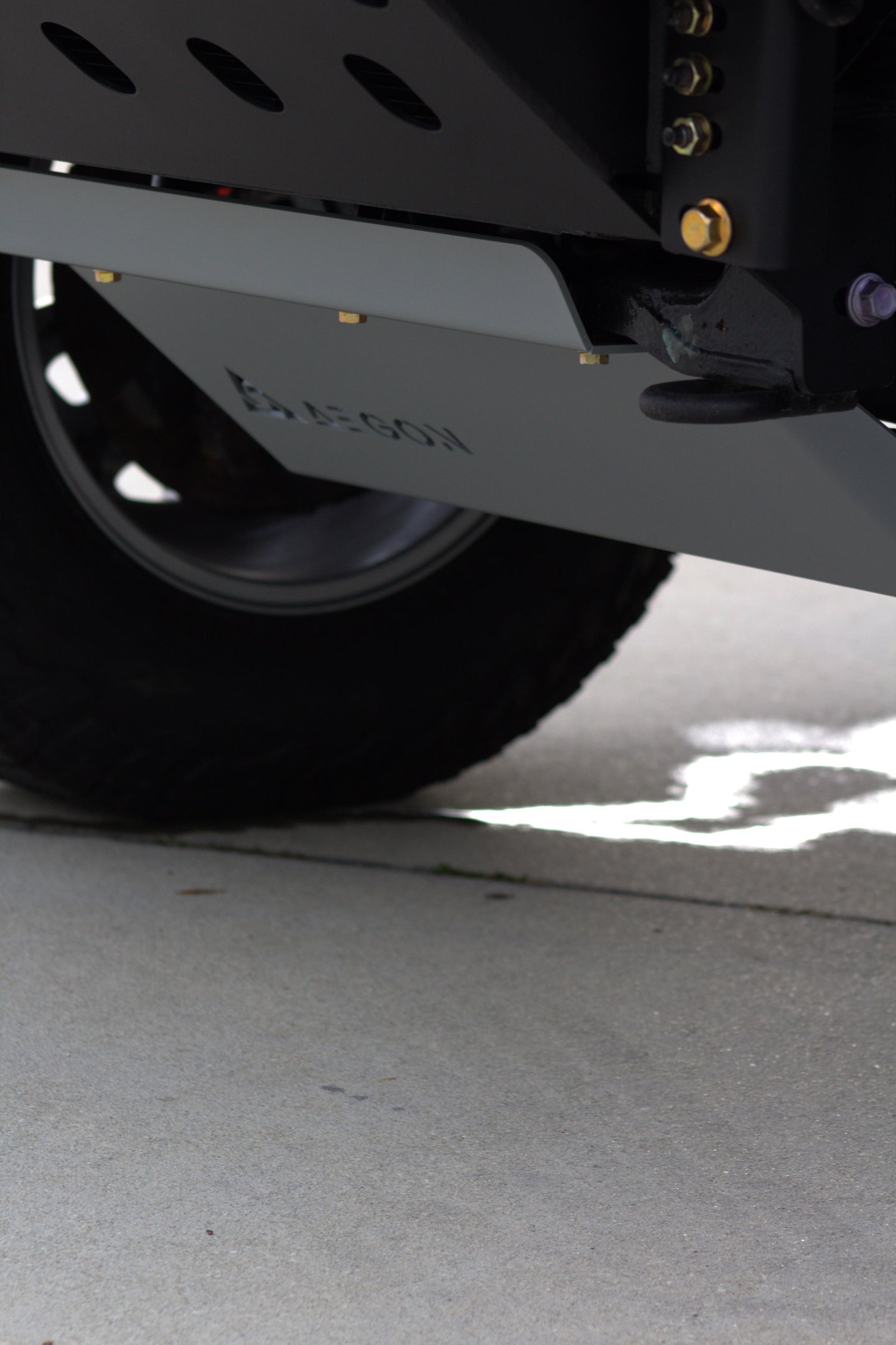 Close-up of a vehicle undercarriage showing a black tire, a dark metal frame, and a gray metal skid plate with the brand name 'Kubota' embossed on it, set on a concrete surface.