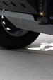 Close-up of a vehicle undercarriage showing a black tire, a dark metal frame, and a gray metal skid plate with the brand name 'Kubota' embossed on it, set on a concrete surface.