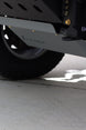 Close-up of a vehicle undercarriage showing a black tire, a dark metal frame, and a gray metal skid plate with the brand name 'Kubota' embossed on it, set on a concrete surface.