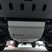 A close-up view from underneath a vehicle showing a white underbody shield with the AEGON logo printed on it, positioned above a gray concrete floor.