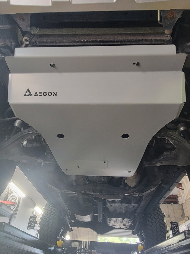 A white metal undercarriage shield with the brand name AEGON printed in black on the left side, installed underneath a vehicle in a garage setting.